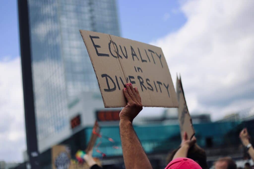 Image taken at an LGBT march or rally with an attendees arm and hand with pin painted fingernails holding a sign saying "equality in diversity"
